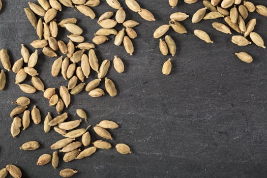 Cardamom seeds spread on slate surface with copy space.