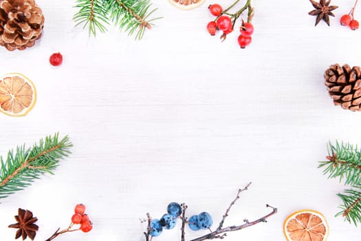 Christmas winter or Happy New Year decoration background. Natur frame composition made from christmas tree branches, pine cones and colorful berries on a rustic white wooden table. Top view copy space.
