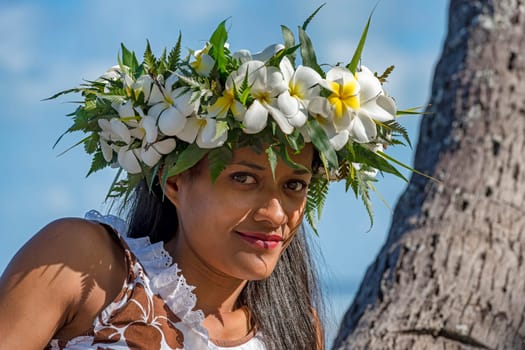 Young woman with flower wreath from Frangipani leans against palm trunk,Raiatea,French Polynesia