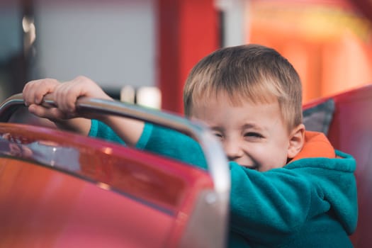 Little cute Caucasian boy sitting inside a roofless car on a carousel in an amusement park