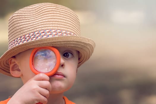 Photo of cute little happy Caucasian boy with a straw hat holding magnifying glass