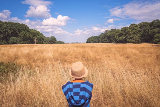 Little boy wearing straw hat standing in front of a yellow grass field