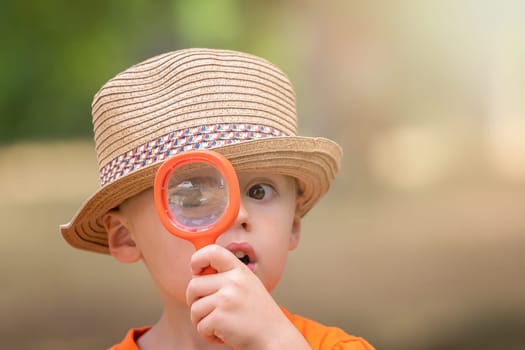 Photo of cute little happy Caucasian boy with a straw hat holding magnifying glass