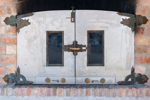 Frontal view on the doors of a bakery oven with brass fittings and windows in a brick wall.