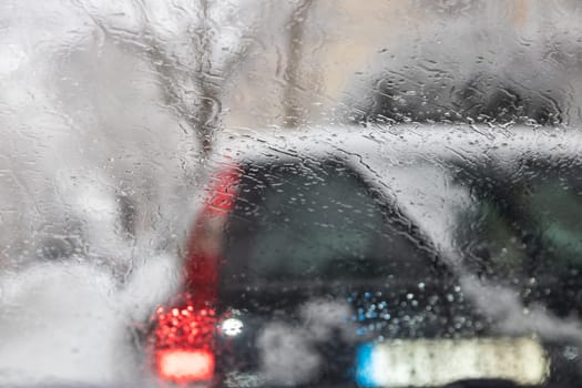 Abstract rain background.  Rain drops on car windshield with red road light bokeh during rainy season.