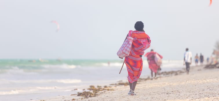 Rear view of traditonaly dressed maasai man walking the sand and selling hand made jewelry on picture perfect tropical Paje beach, Zanzibar, Tanzania, East Africa.