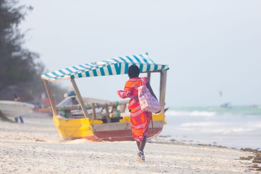 Rear view of traditonaly dressed maasai man walking the sand and selling hand made jewelry on picture perfect tropical Paje beach, Zanzibar, Tanzania, East Africa.