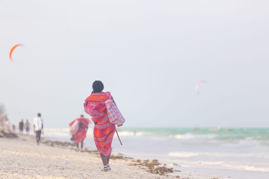 Rear view of traditonaly dressed maasai man walking the sand and selling hand made jewelry on picture perfect tropical Paje beach, Zanzibar, Tanzania, East Africa.