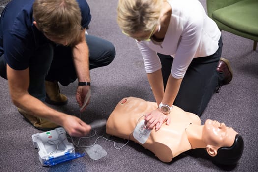 CPR training medical procedure workshop. Demonstrating chest compressions and use of AED automatic defibrillator on CPR doll.