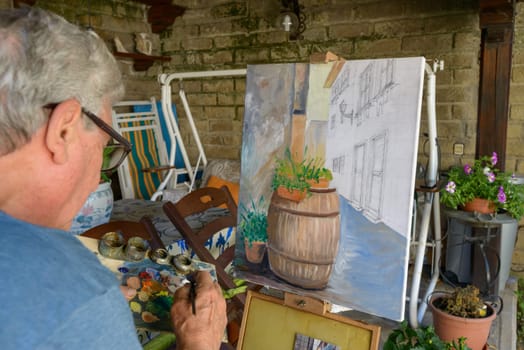 Senior Man painting a picture with oil colors choosing the color on the palette