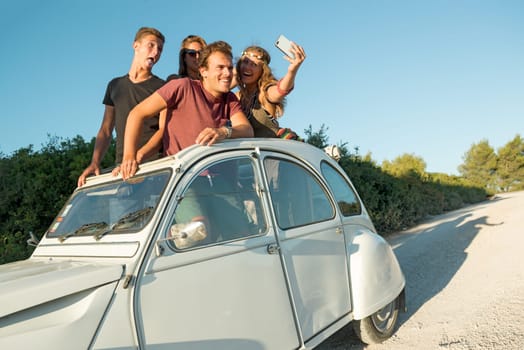 Group of happy people taking a selfie in a car at sunset in summer.