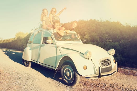 Group of happy friends in a car at sunset in summer.