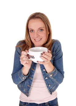 A young woman in a jeans jacket standing and holding a big mug of hot.sup on a cold winter day, isolated for white background.