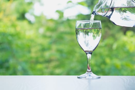 Female hand pouring water from bottle to glass on nature background