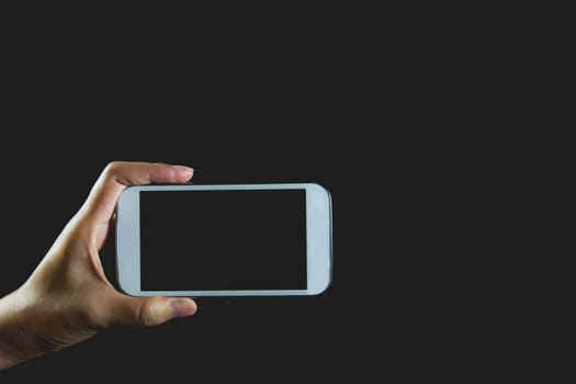 Woman hand holding smart phone isolated on dark background.
