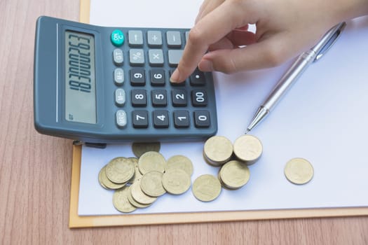 Hand of woman are pressing the calculator with stack coins on the table. Man pressing calculator button. Financial analyzing concept.