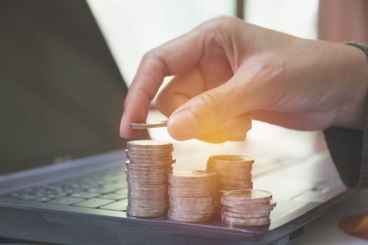 Hand with stack coins on laptop. Financial, accounting and saving concept.
