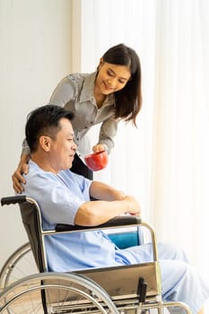Elderly patient with red cup coffee and his relative on wheelchair is looking through the window