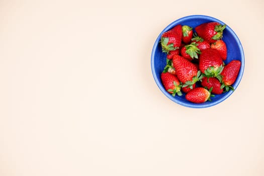 strawberries in blue bowl on pastel orange ground from above