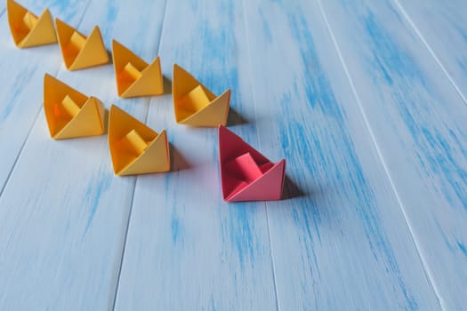 Leadership concept, red leader boat, standing out from the crowd of orange boats, on wooden background