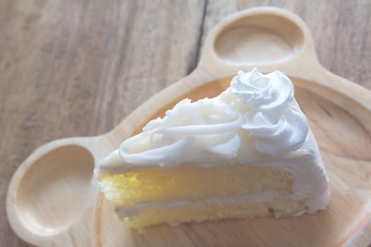 Piece of white cake on wooden dish and wooden table.