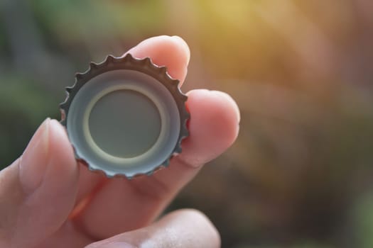Hand holding a bottle caps on nature background.