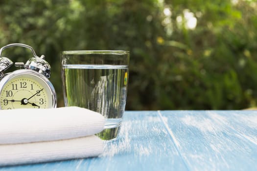 Water in glass with alarm clock and handkerchief on nature background.
