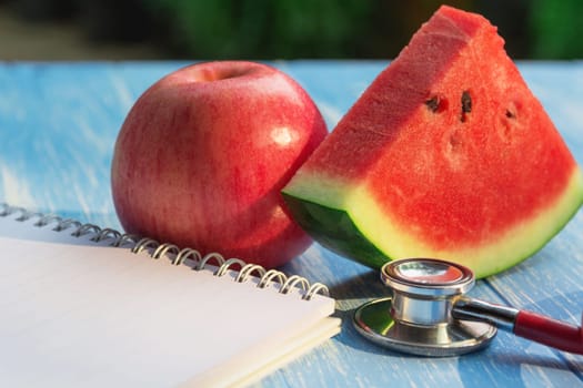 Stethoscope, apple, watermelon and note on blue and wooden table for health concept.