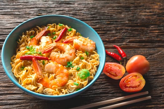 Top view of instant noodles with shrimp and chopsticks on wooden background.