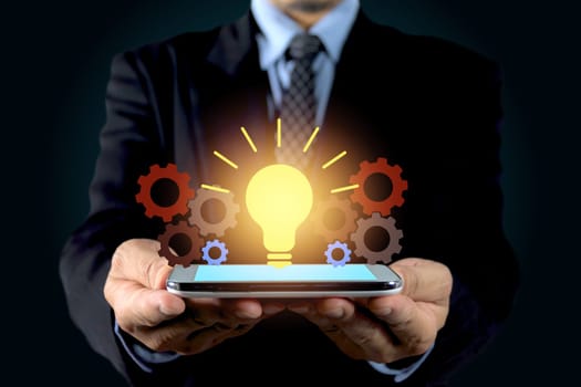 Double exposure close up of businessman hands holding glass light bulb with smart phone.