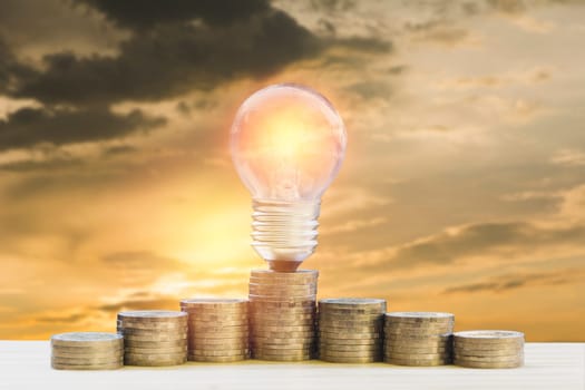 Energy saving light bulb and tree growing on stacks of coins on nature background. Saving, accounting and financial concept.