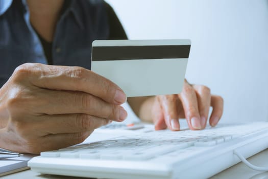 Hands holding blue credit card and using a computer for online shopping concept.