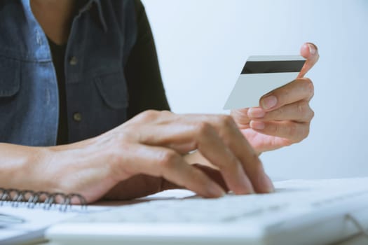 Hands holding blue credit card and using a computer for online shopping concept.