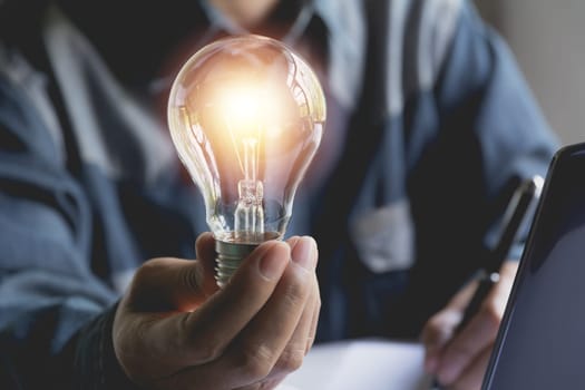 Hand of male holding a light bulb and using a laptop for accounting and creative concept.