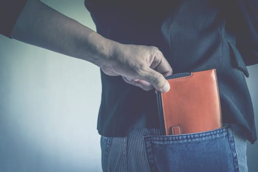 Close-up of a the hand of thief stealing the wallet to a woman. Thief stealing wallet from back pocket of a woman.