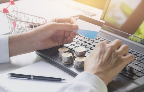 Hands holding blue credit card and using a laptop for online shopping concept.