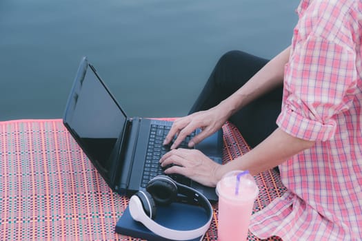 A woman using laptop computer while sitting beside river.