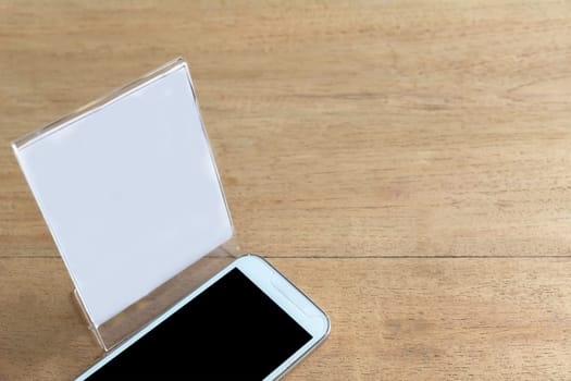 Smart phone with white paper on wooden table background. Technology and communication concept.