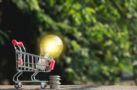 Energy saving light bulb with coins and shopping cart for saving, financial and shopping concept.