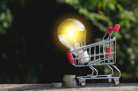 Energy saving light bulb with coins and shopping cart for saving, financial and shopping concept.