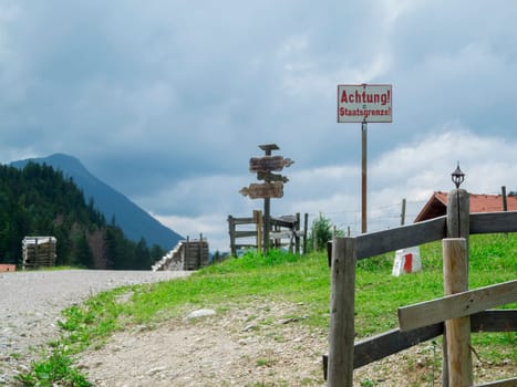 Schwangau, Germany - July 11, 2018: Border sign and landmark between Germany and Austria on the Salober-Alm photographed from Germany.  Border sign and landmark with weathered wooden signposts between Germany and Austria in summer at the Salober Alm at cloudy sky.
