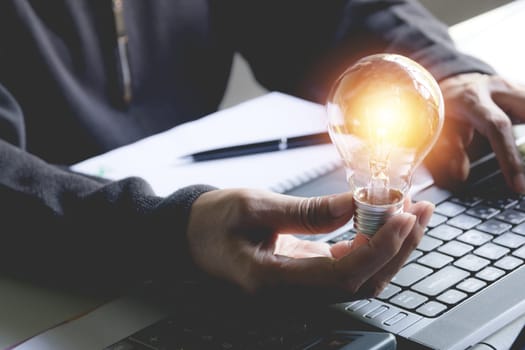 Hand of male holding a light bulb and using a laptop for accounting and creative concept.