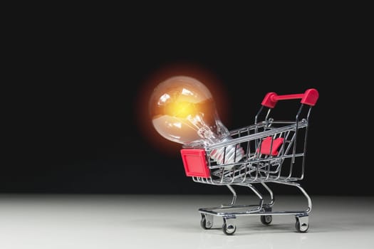 Energy saving light bulb with stacks of coins and shopping cart for saving, financial and shopping concept.