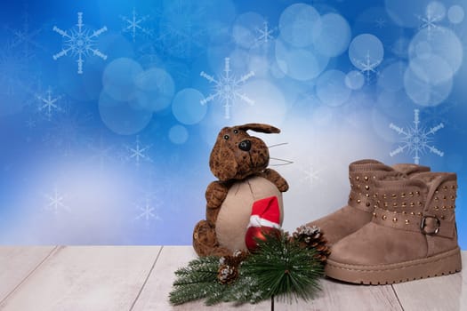 Christmas background. Table top christmas winter decoration background with an pair of winter boots and xmas tree fir branches and a funny dog over beautiful abstract blue christmas background. Space for design. Card concept.
