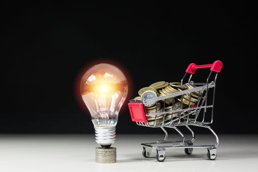 Energy saving light bulb with stacks of coins and shopping cart for saving, financial and shopping concept.