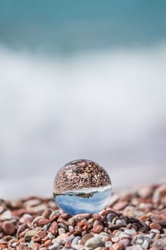 Historical Sveti Stefan old town reflected in large transparent glass ball placed on peebles on the beach, coast of Montenegro
