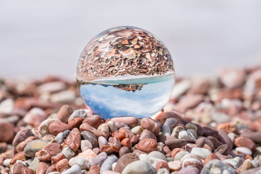Historical Sveti Stefan old town reflected in large transparent glass ball placed on peebles on the beach, coast of Montenegro