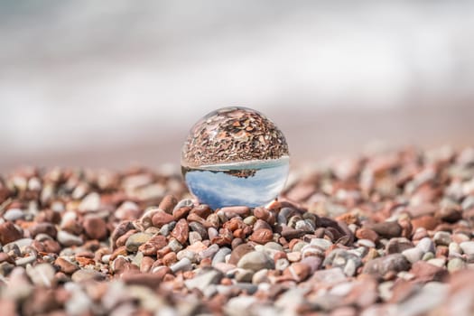 Historical Sveti Stefan old town reflected in large transparent glass ball placed on peebles on the beach, coast of Montenegro