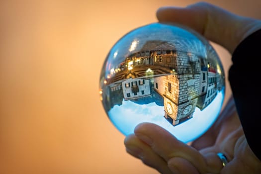Man holding transparent glass ball reflecting the old Clock tower and square in Kotor Old Town, Montenegro
