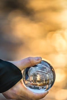 Man holding transparent glass ball reflecting the old Clock tower and square in Kotor Old Town, Montenegro